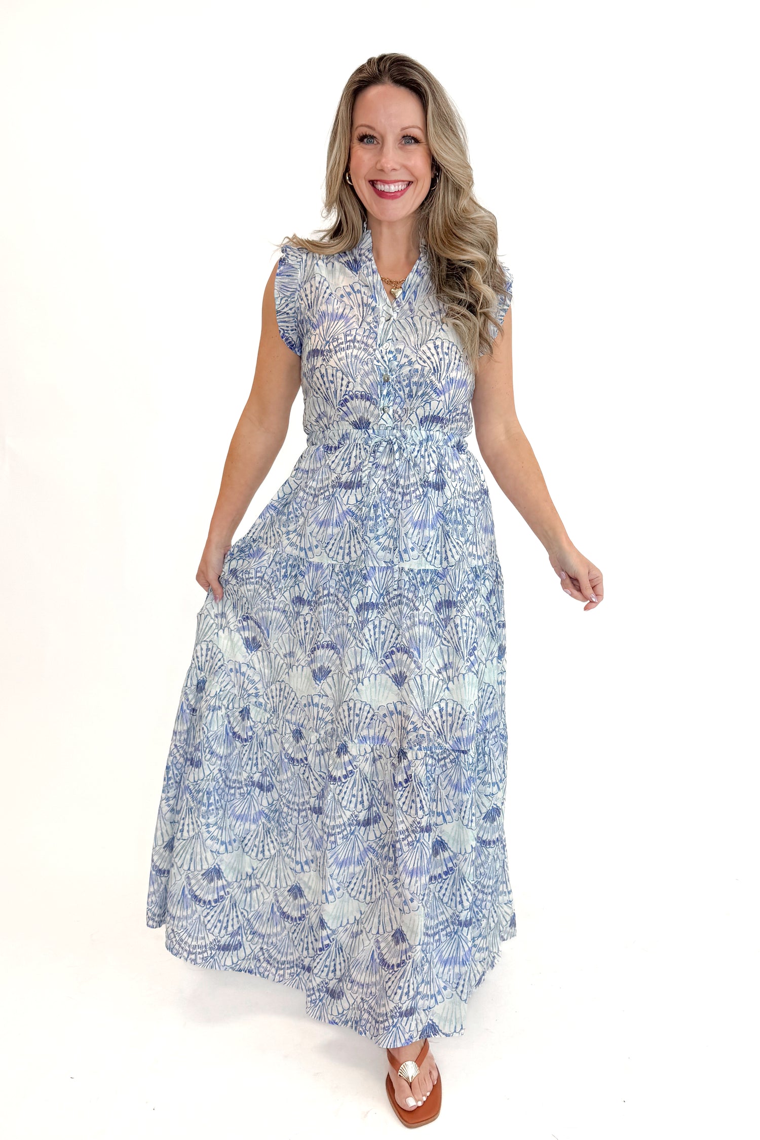 Front view of woman wearing Blue Shell Print Tiered Maxi Dress by PINCH with sandals against white studio background.