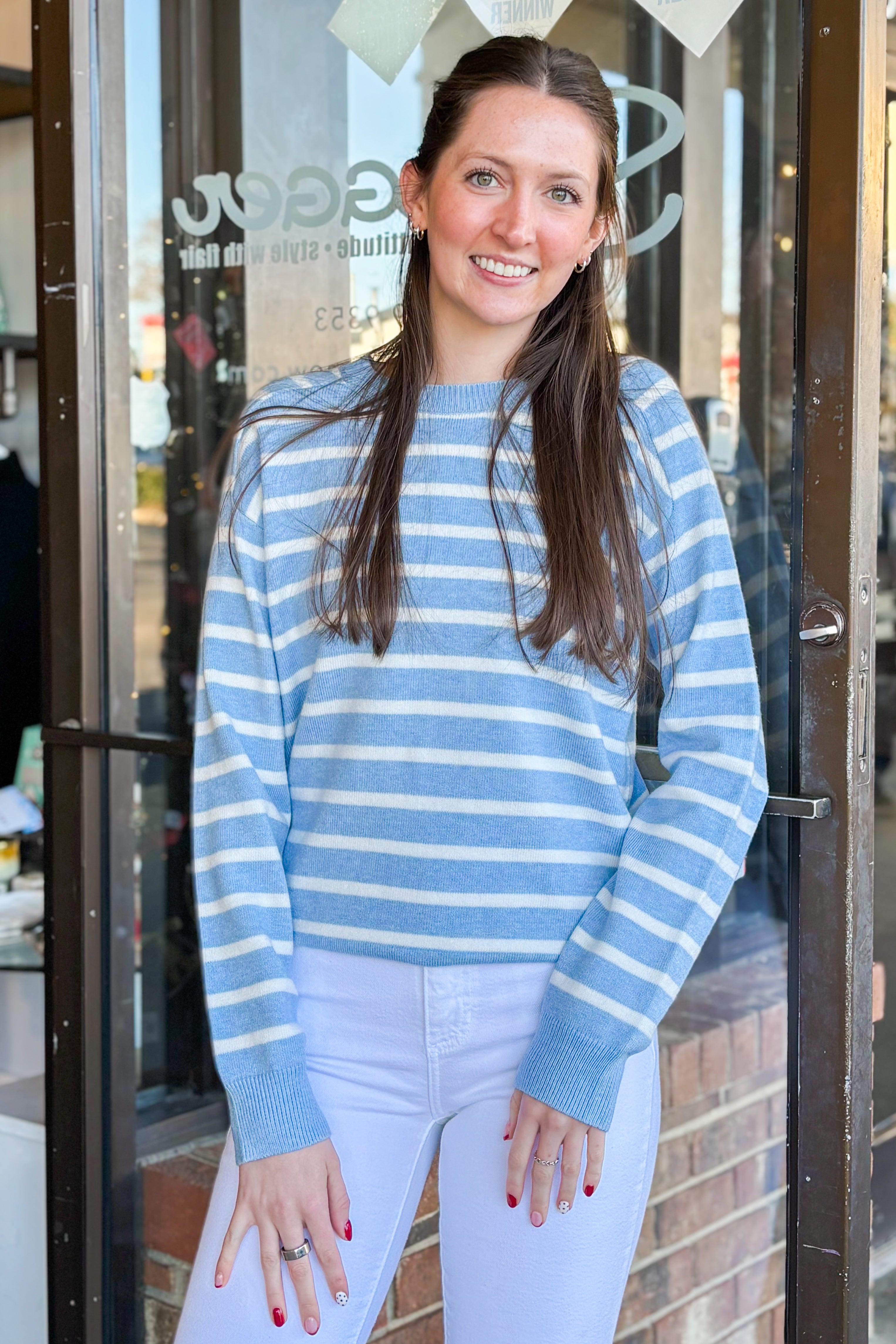 Front view of woman wearing Light Blue Striped Sweater with jeans at a boutique.