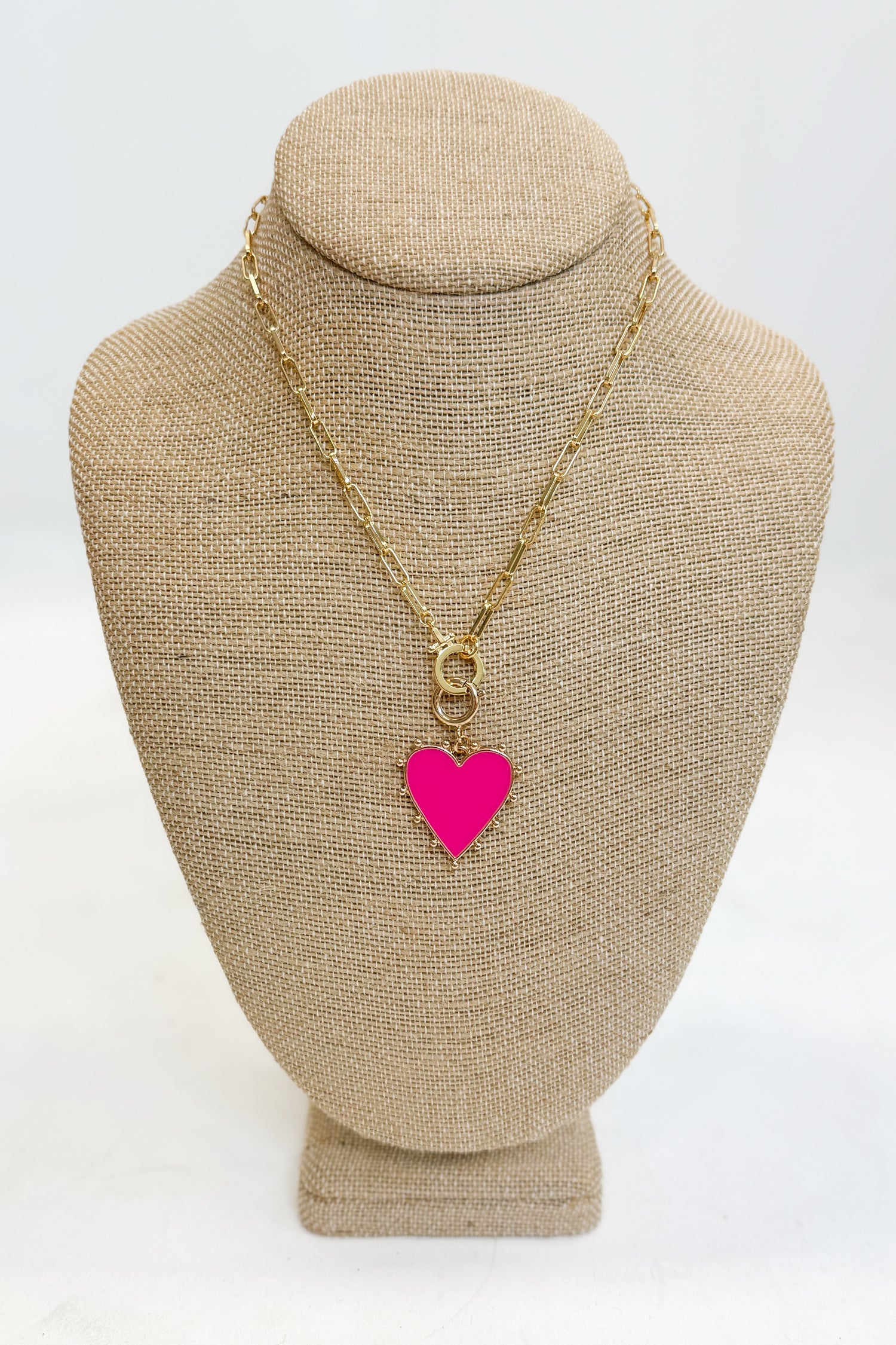 Gold necklace with a pink heart pendant on a beige bust against a white background
