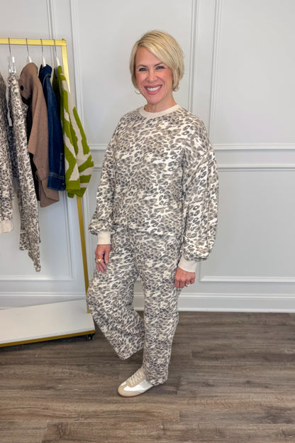 Side view of woman wearing Swagger Boutique’s Taupe Leopard Sweatpants and Sweatshirt with clothing hanging in the background.
