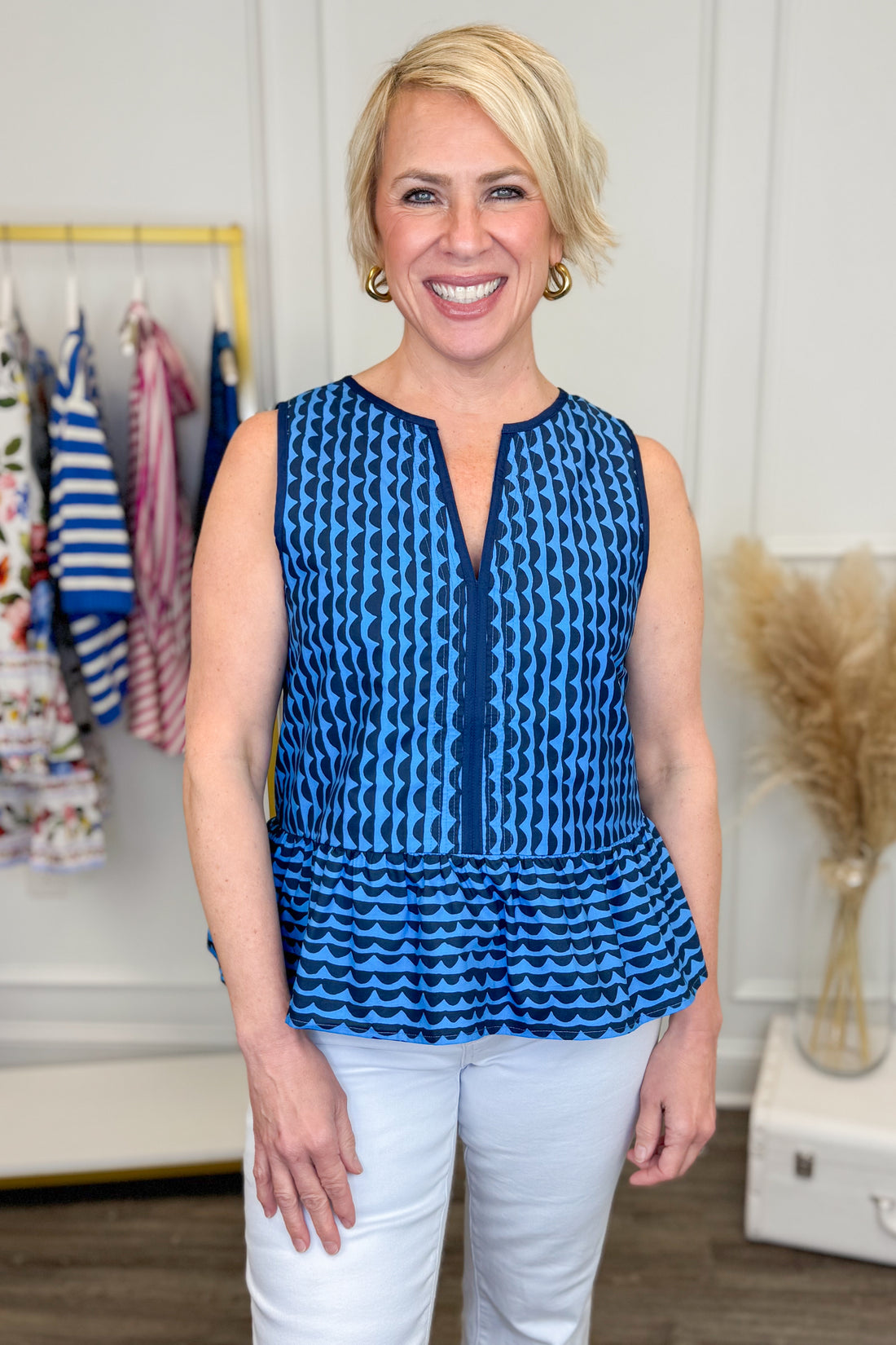 Front view of woman wearing Blue &amp; Navy Scallop Print Peplum Top with white jeans and clothes in the background.