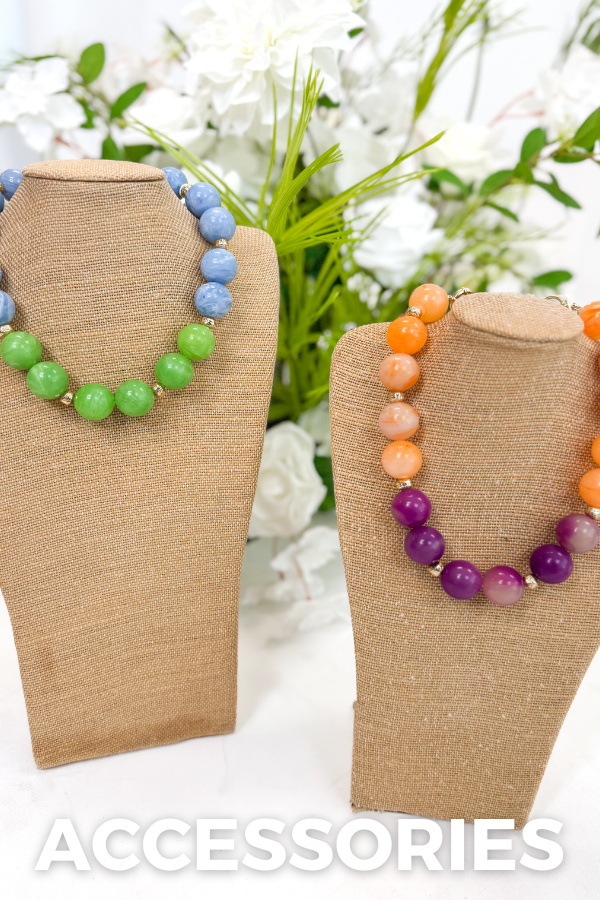 Two necklaces on brown stands with colorful beads against a floral background, labeled 'Accessories'.