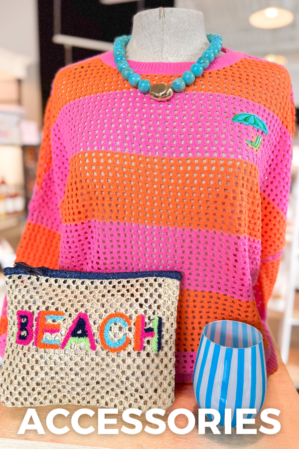 Mannequin wearing a colorful crochet sweater with accessories including a beaded necklace, striped bag, and 'BEACH' pouch.