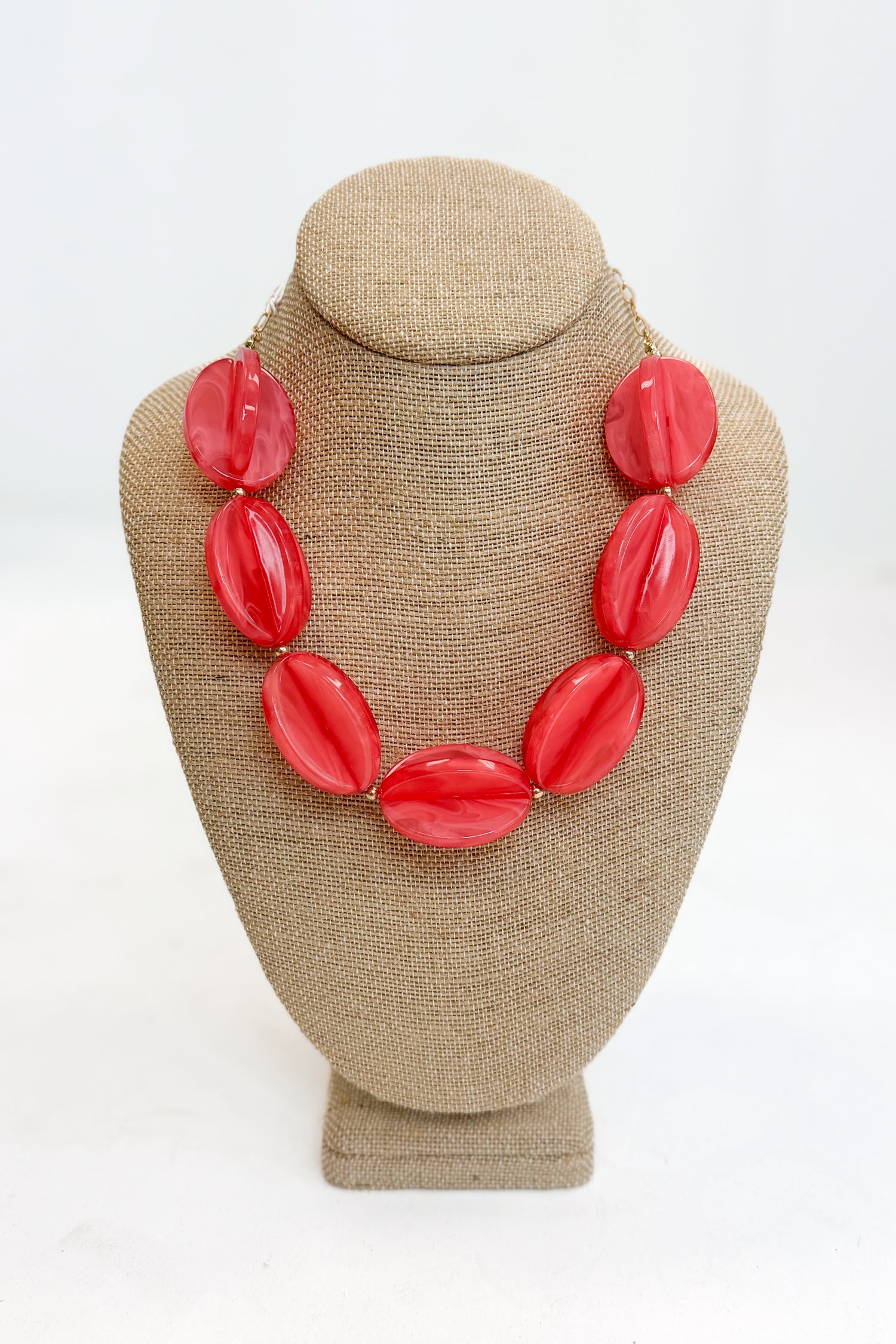 Coral necklace on a beige bust against a white background