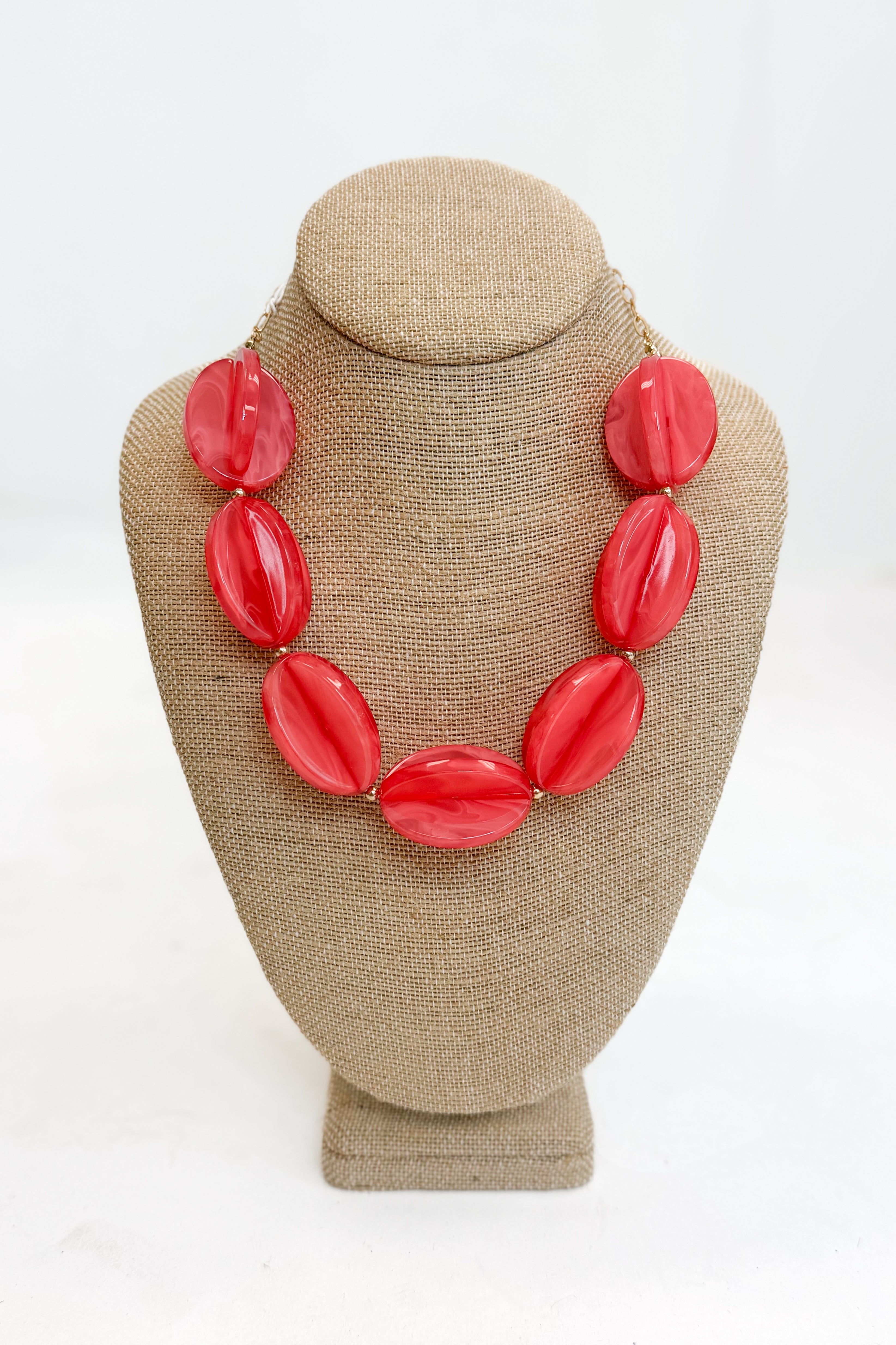 Coral necklace on a beige bust against a white background