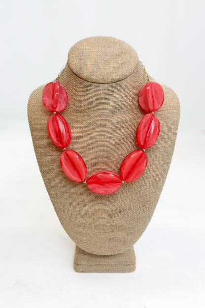 Coral necklace on a beige bust against a white background