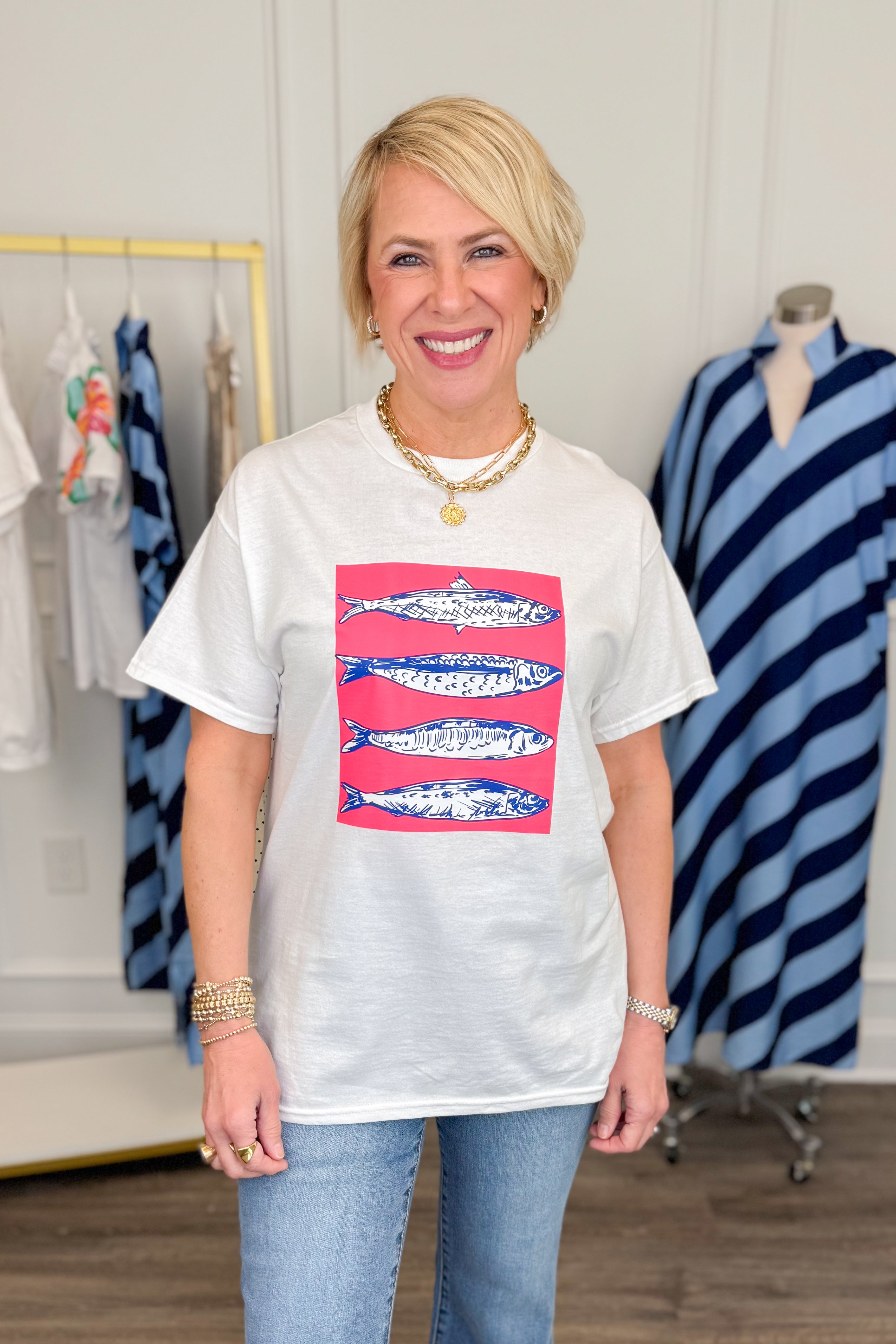 Woman wearing a white t-shirt with a graphic design of fish on a pink background, standing in a clothing store.