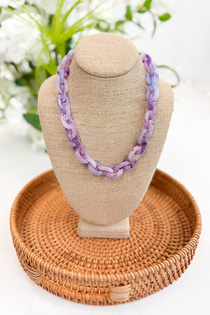 Necklace on a beige bust with a woven basket stand, against a blurred floral background