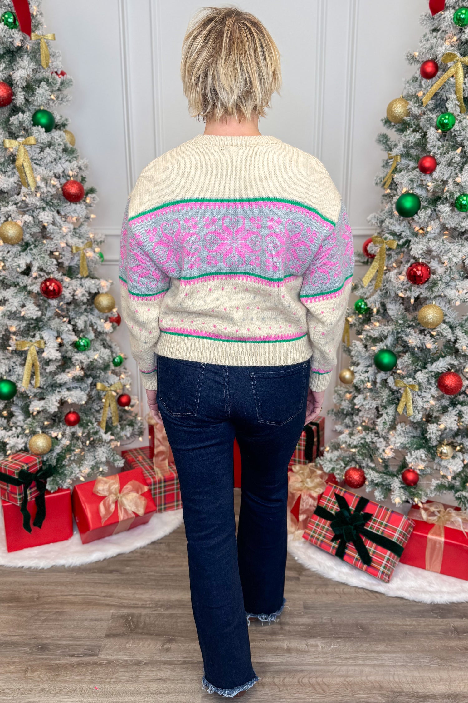 Person wearing a colorful sweater in front of decorated Christmas trees with presents.