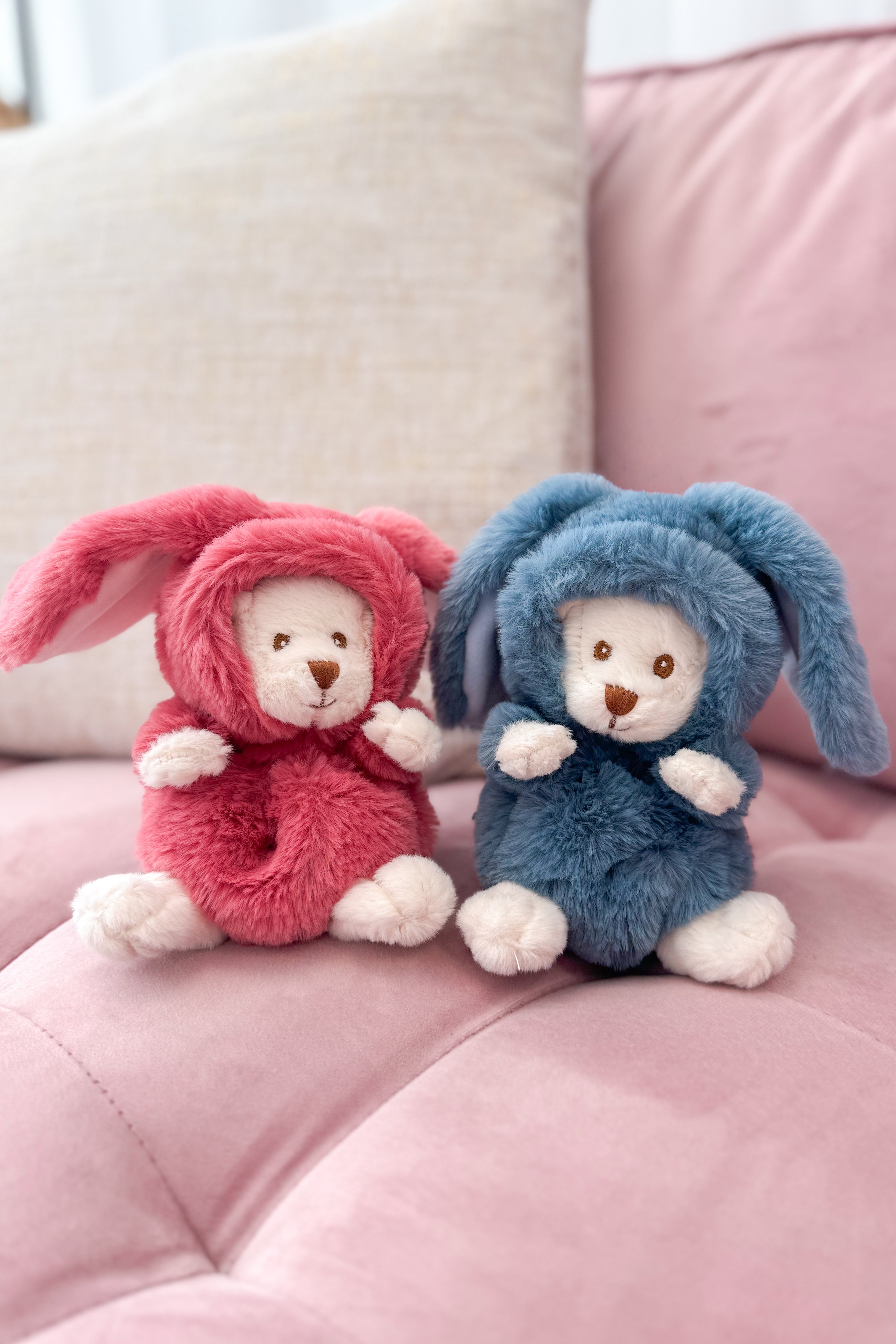 Two plush toys, one in pink and one in blue, sitting on a pink surface.