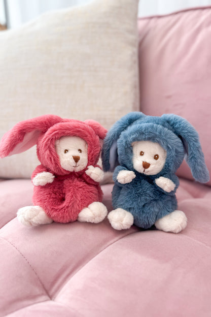 Two plush toys, one in pink and one in blue, sitting on a pink surface.