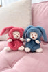 Two plush toys, one in pink and one in blue, sitting on a pink surface.
