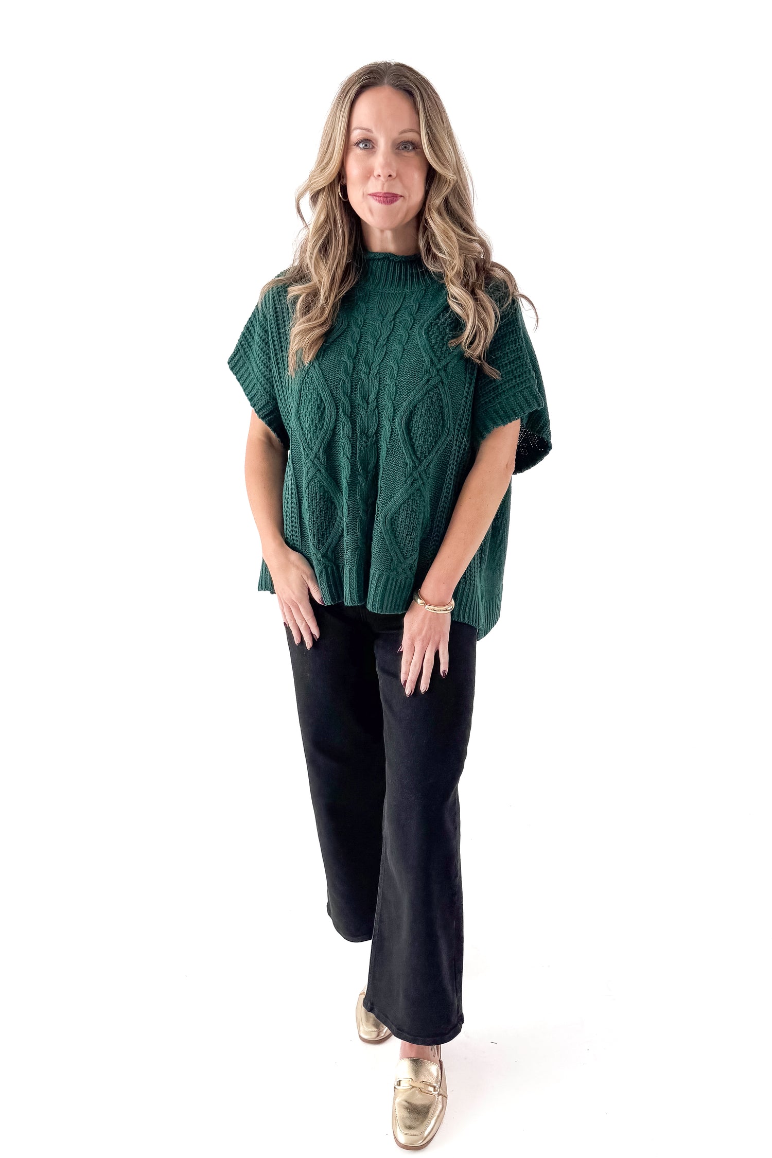 Front view of woman wearing Green Claude Cable Knit Sweater with jeans against white studio background.