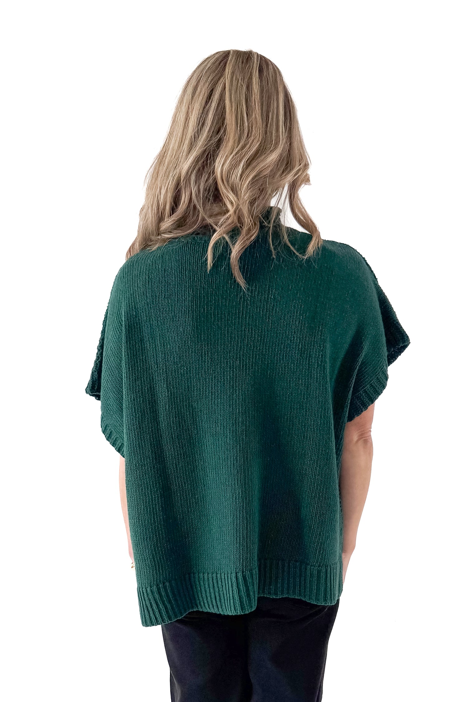 Back view of woman wearing Green Claude Cable Knit Sweater with jeans against white studio background.