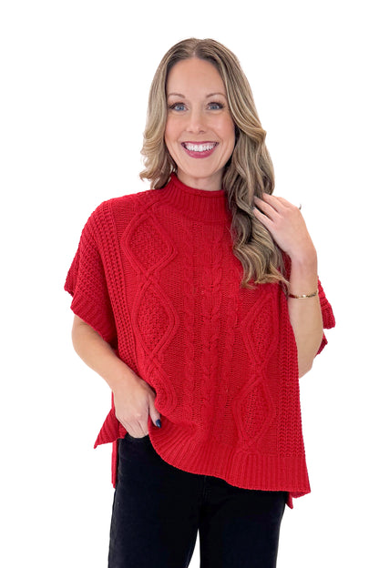 Front view of woman wearing Red Claude Cable Knit Sweater by MudPie with jeans against white studio background.