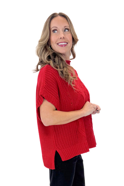 Side view of woman wearing Red Claude Cable Knit Sweater by MudPie with jeans against white studio background.