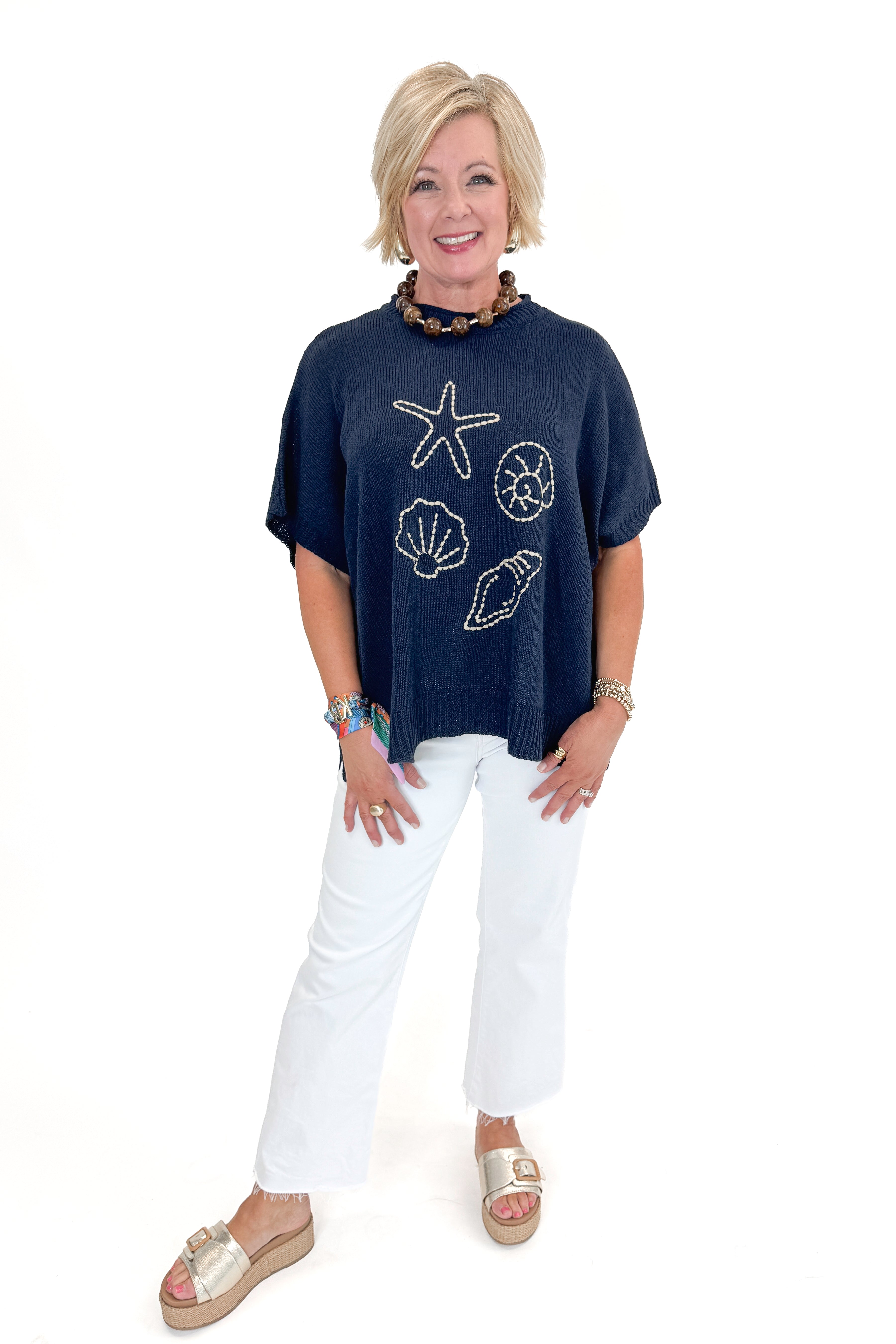 Front view of woman wearing Navy Hurley Beach Sweater by MudPie with jeans against white studio background.