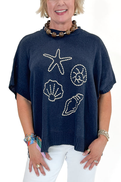 Front detail view of woman wearing Navy Hurley Beach Sweater by MudPie with jeans against white studio background.