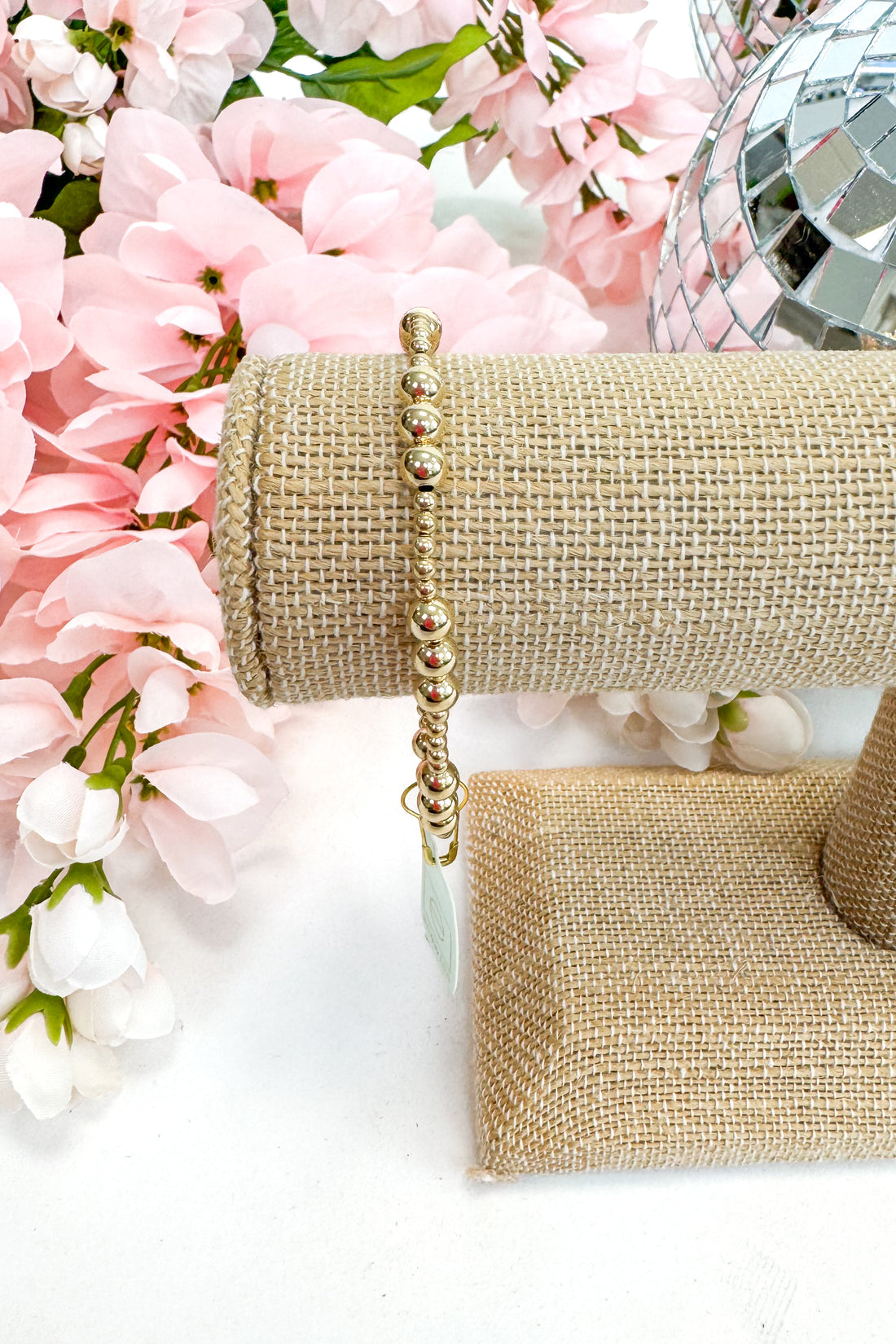 gold enewton bracelet on burlap display with floral background