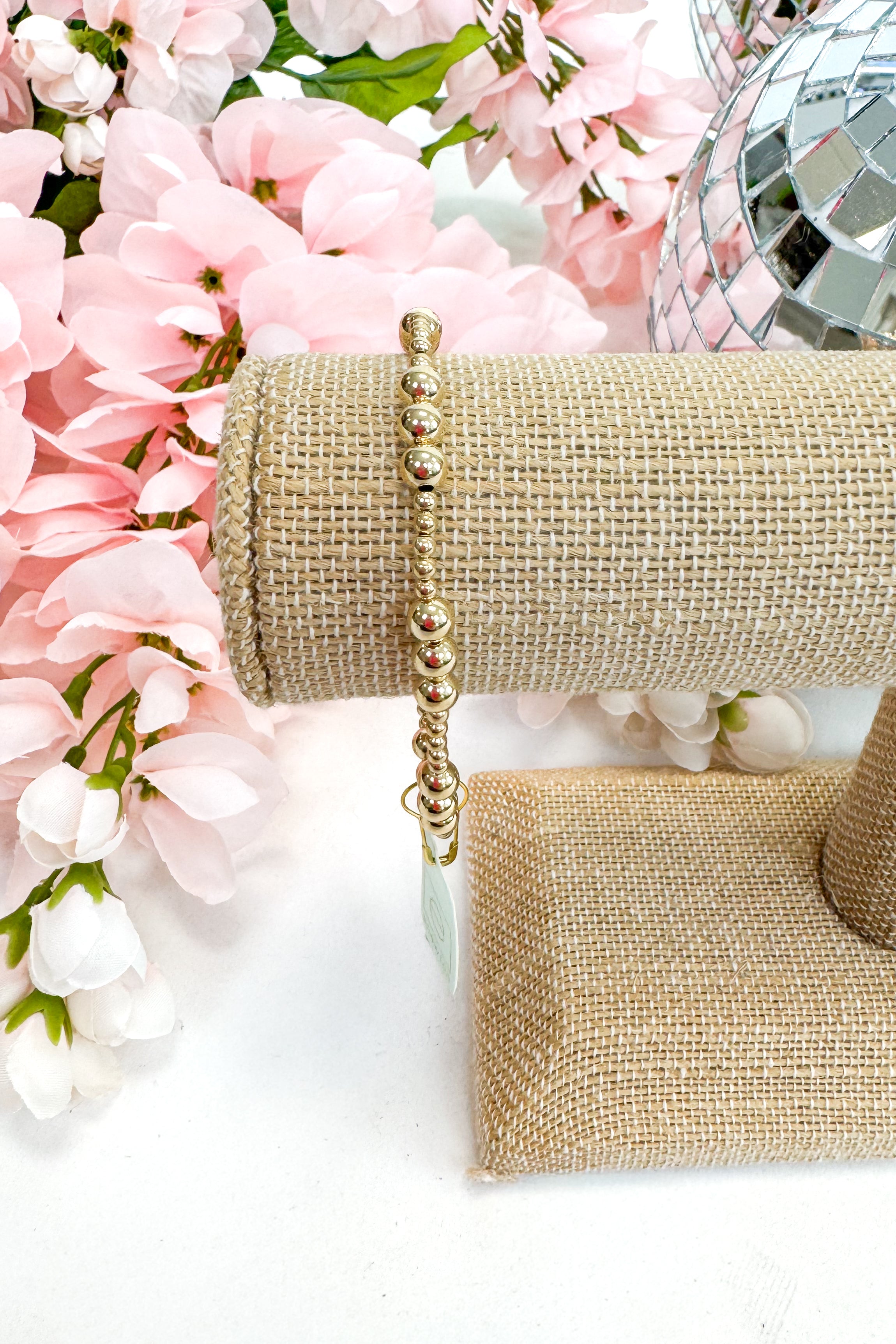 gold enewton bracelet on burlap display with floral background