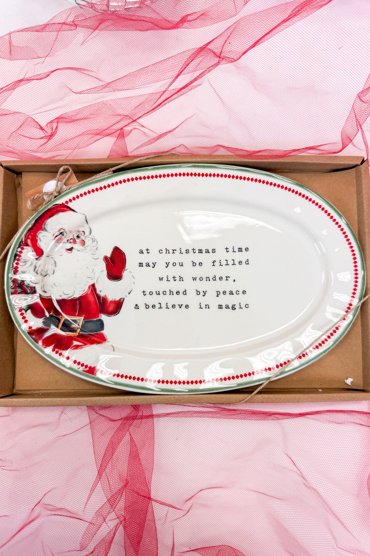 Decorative plate with Santa Claus design and text, placed on pink fabric.