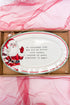 Decorative plate with Santa Claus design and text, placed on pink fabric.