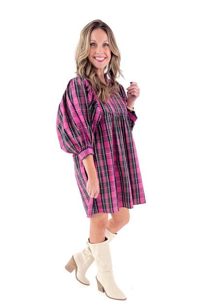 Side view of woman wearing Shipley pink plaid dress against white studio background.