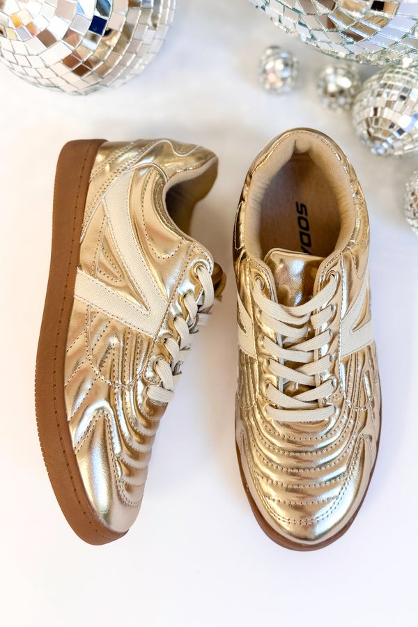 Pair of gold sneakers with decorative patterns on a white background with disco balls.