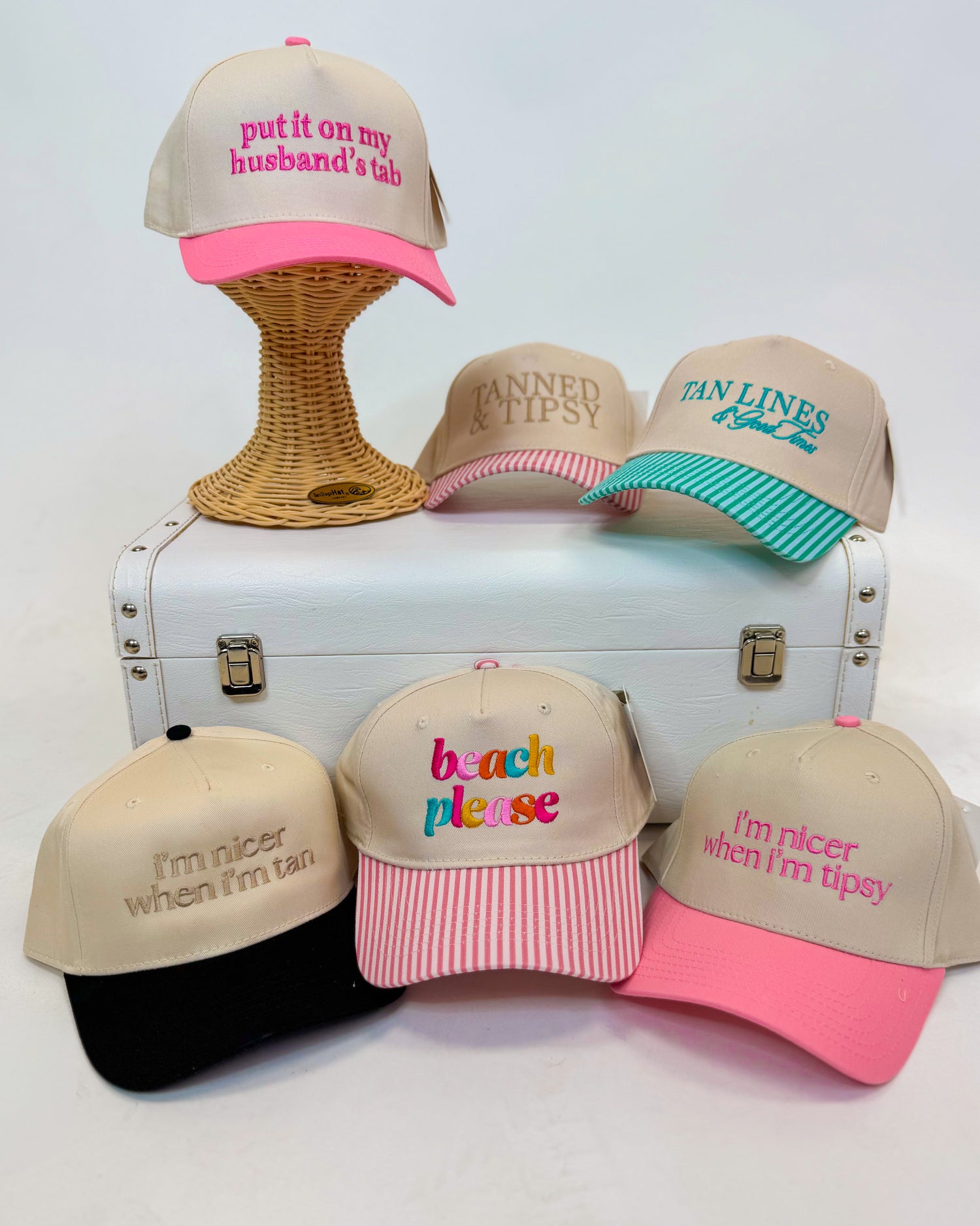 Collection of tan baseball caps with colorful text on a white surface with a suitcase.