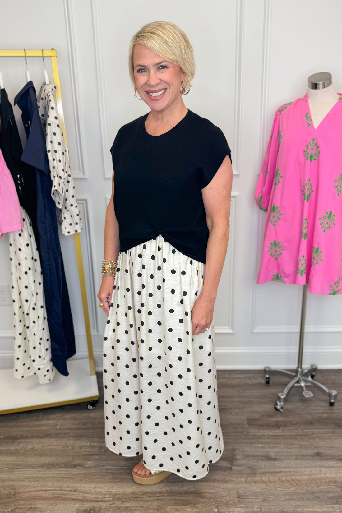 Side view of woman wearing Swagger Boutique’s Black &amp; Cream Polka Dot Layered Midi Dress by Entro with sandals at the store. 