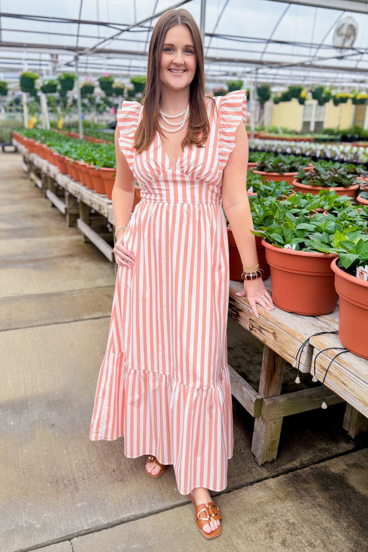 Front view of woman wearing Coral Striped Tie Back Maxi Dress by Skies Are Blue at a garden center