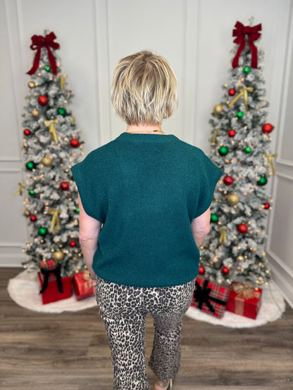 Person wearing a green shirt and leopard print pants standing in front of two decorated Christmas trees.