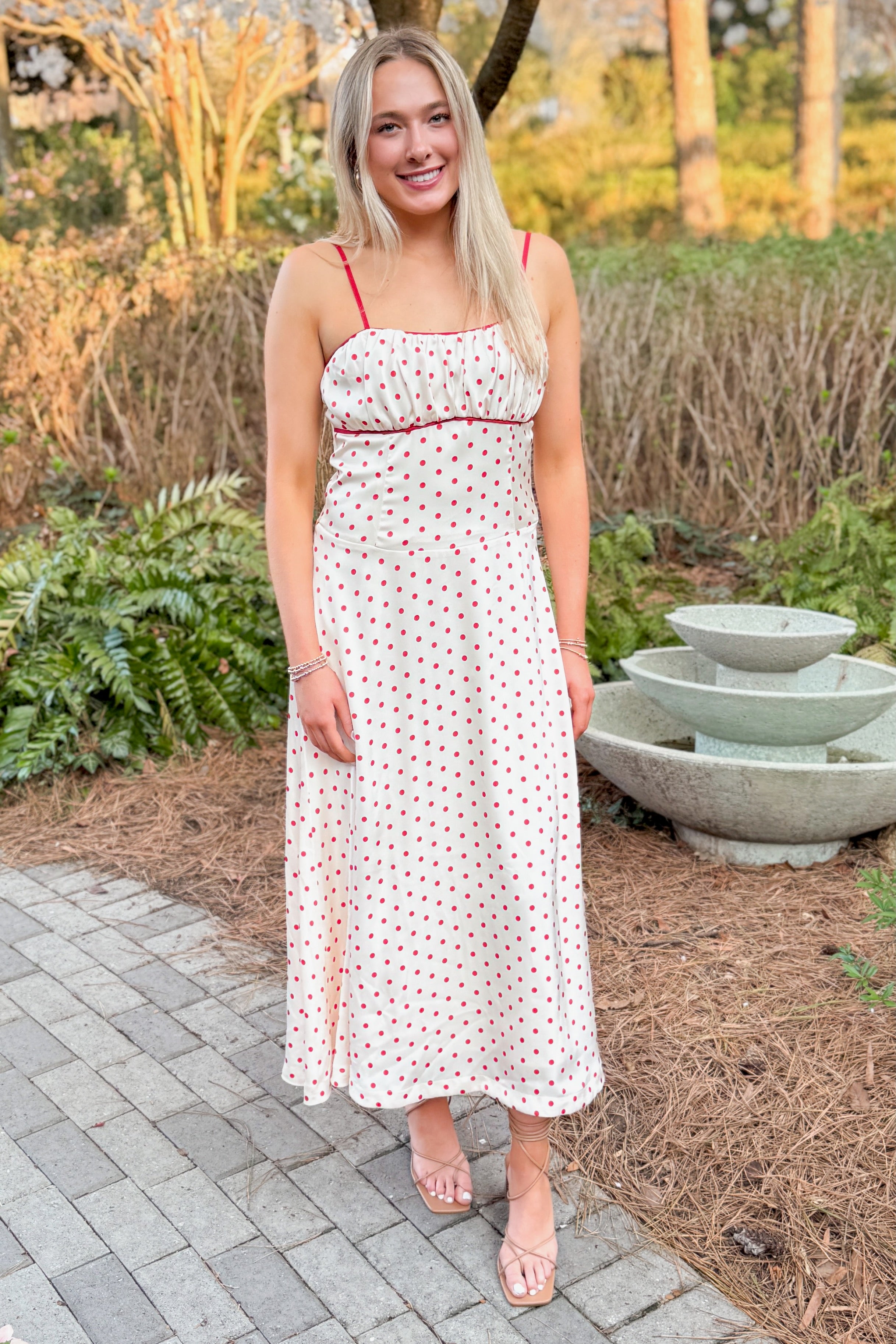 Front view of woman wearing Cream &amp; Red Polka Dot Midi Dress by Skies Are Blue outside at a garden.