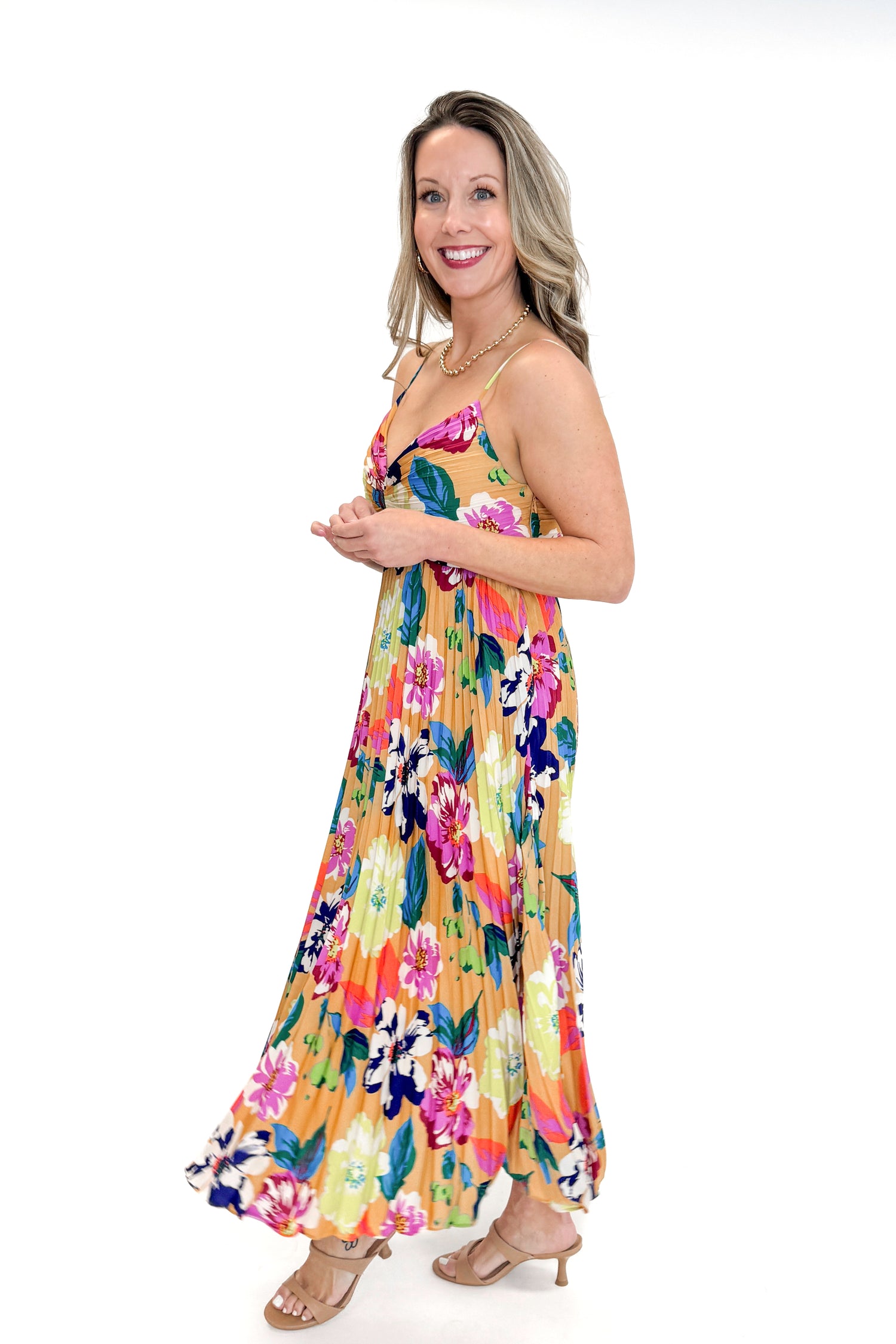 Side view of woman wearing Taupe &amp; Multi Floral Print Pleated Midi Dress by Skies Are Blue against white studio background.