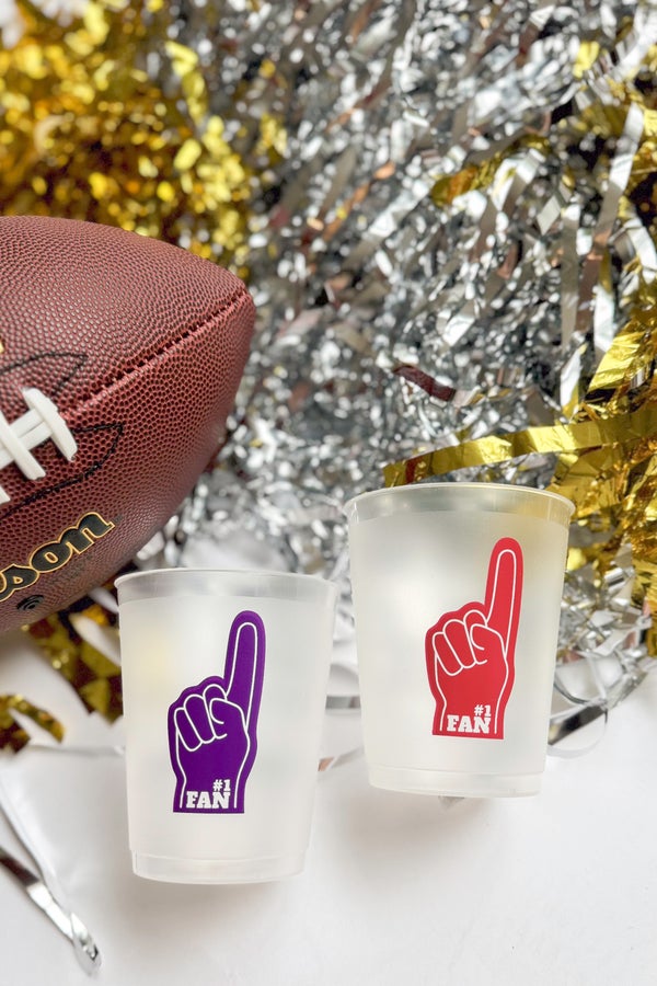 Two frosted glasses with foam finger designs next to a football and festive decorations.