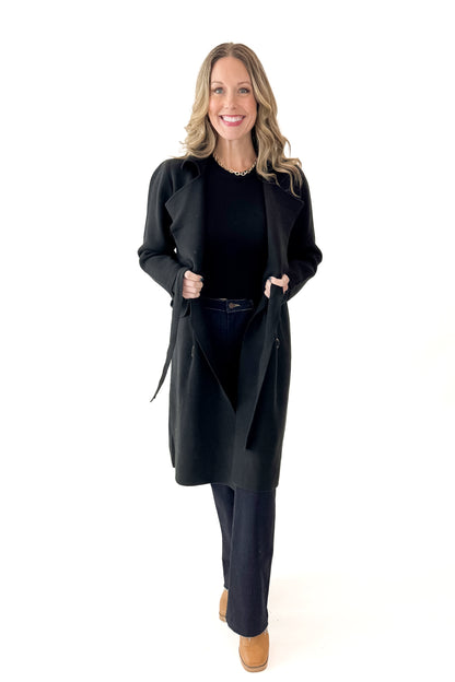Front view of woman wearing Black Long Peacoat with jeans against white studio background.