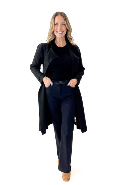 Front view of woman wearing Black Long Peacoat with jeans against white studio background.