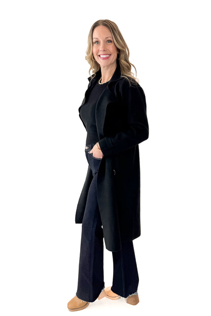 Side view of woman wearing Black Long Peacoat with jeans against white studio background.