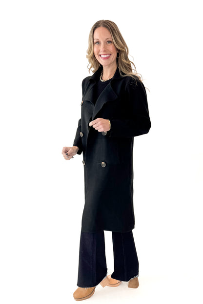 Side view of woman wearing Black Long Peacoat with jeans against white studio background.