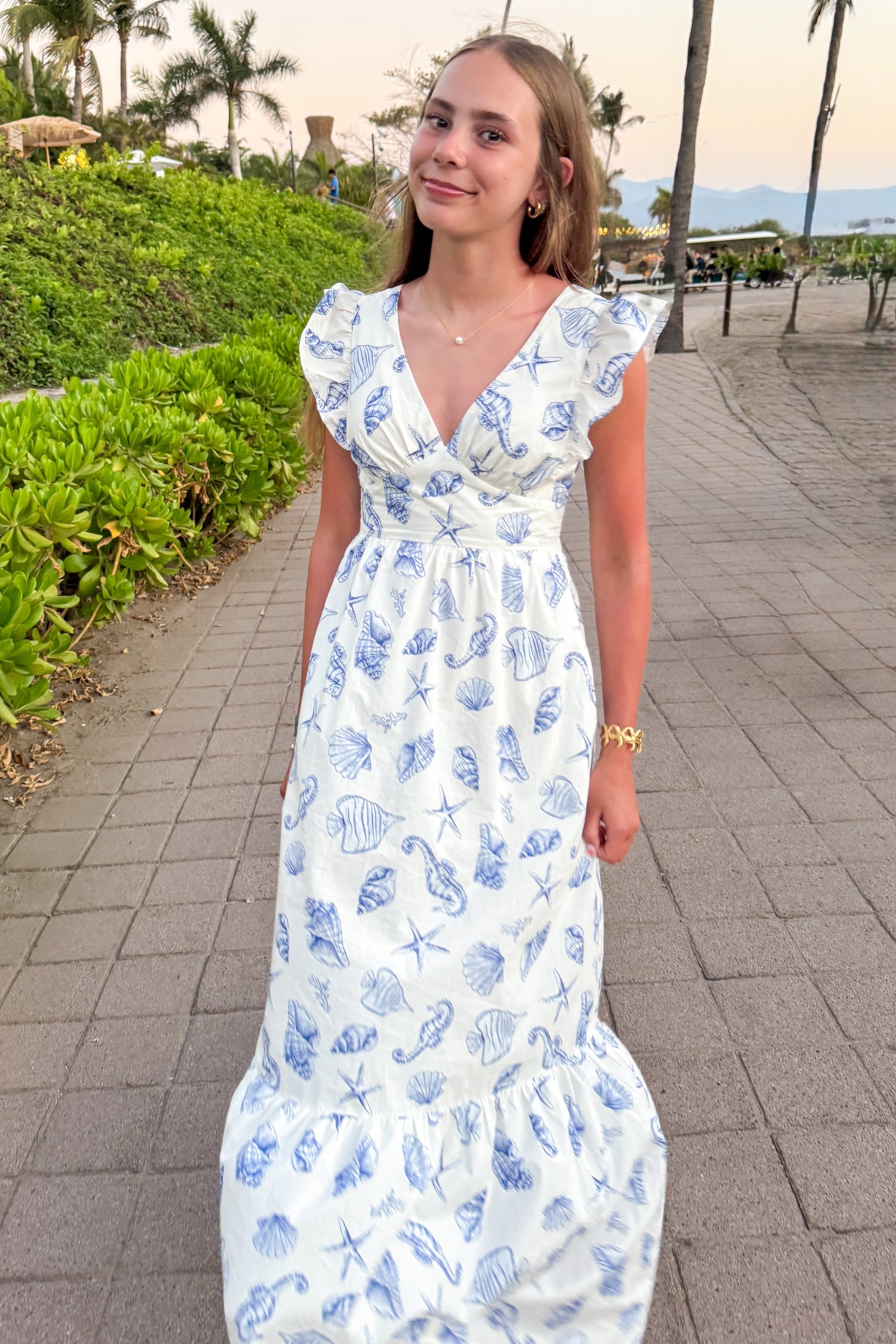 Front view of woman wearing White &amp; Blue Shell Print Tie Back Maxi Dress by Skies Are Blue outside at the beach.