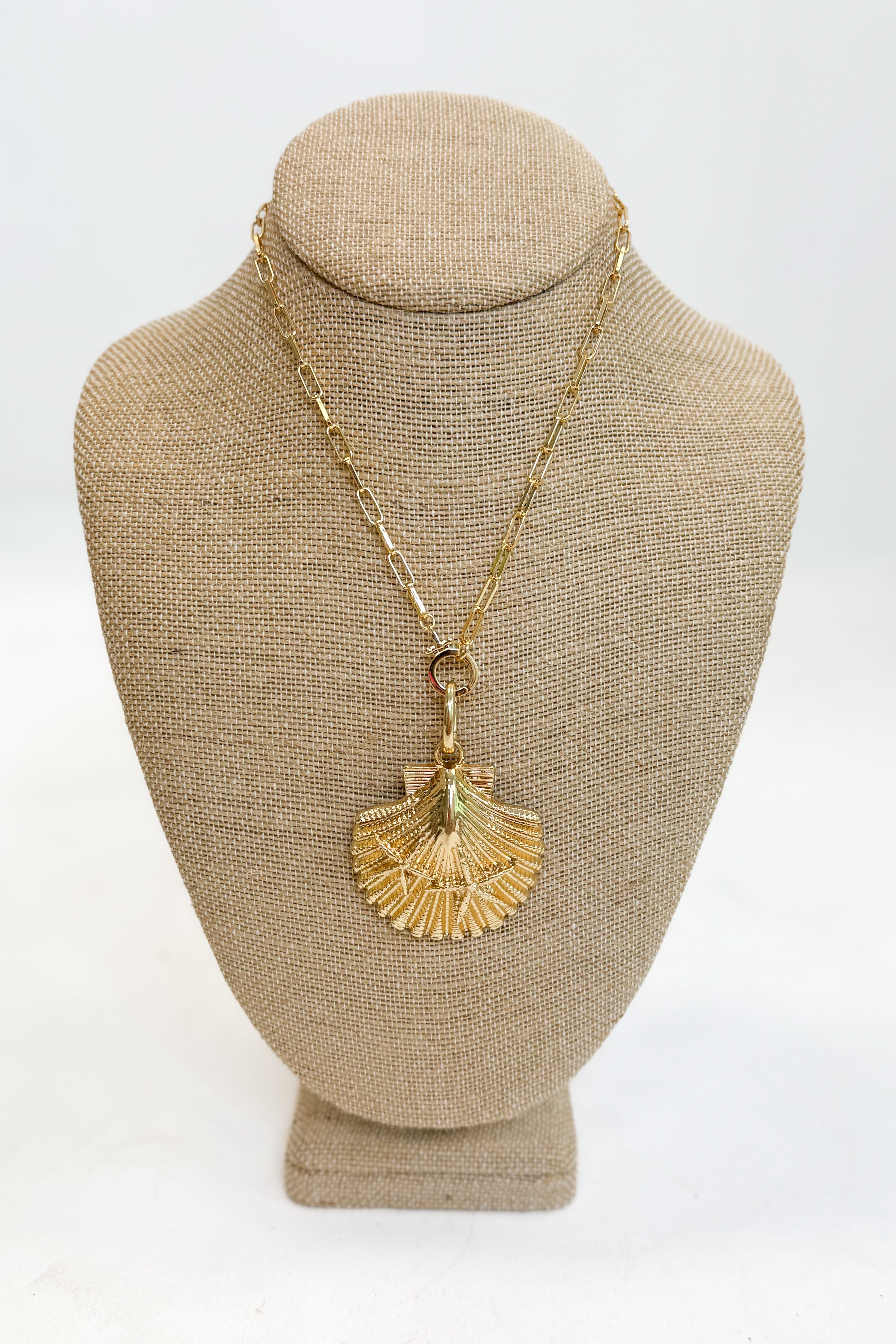 Gold necklace with a shell pendant on a beige bust against a white background