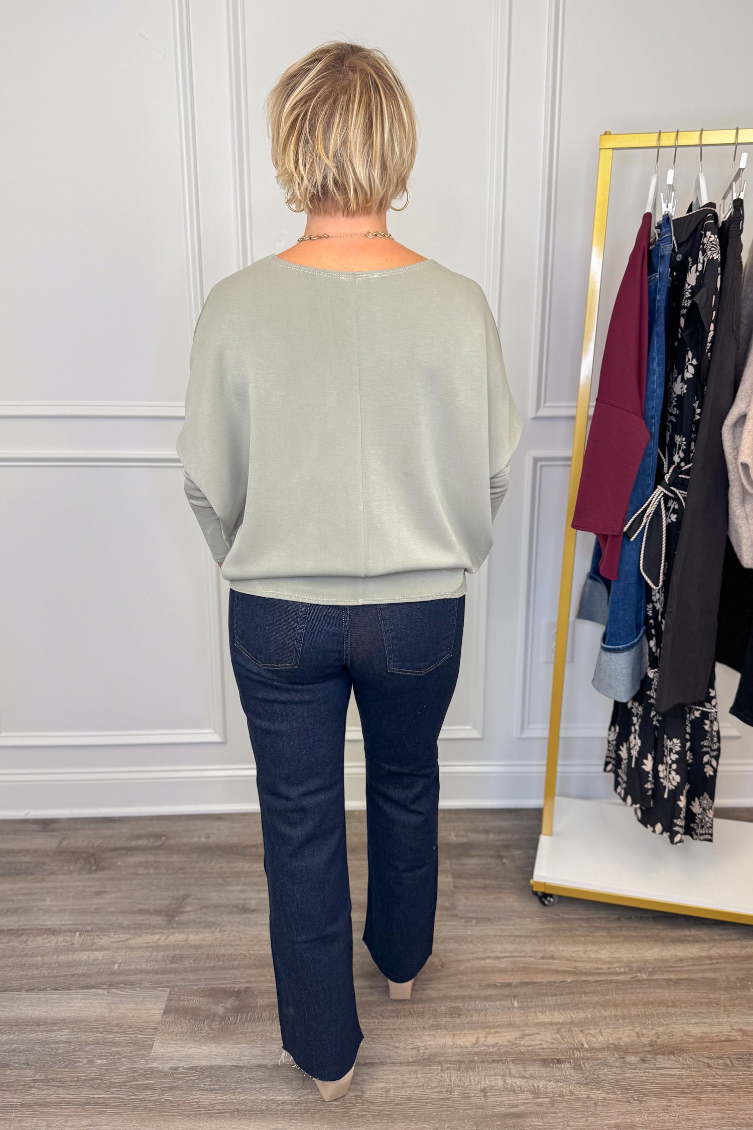 Person wearing a light gray sweater and dark blue jeans standing in front of a clothing rack.