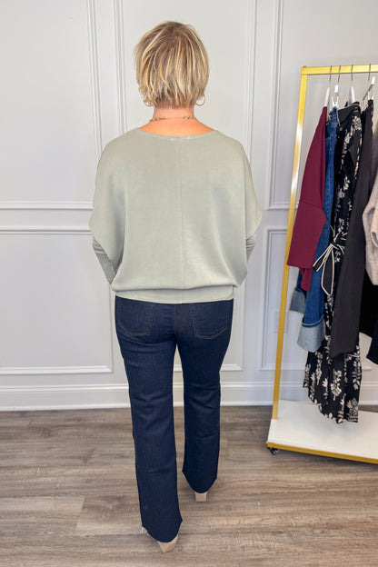 Person wearing a light gray sweater and dark blue jeans standing in front of a clothing rack.