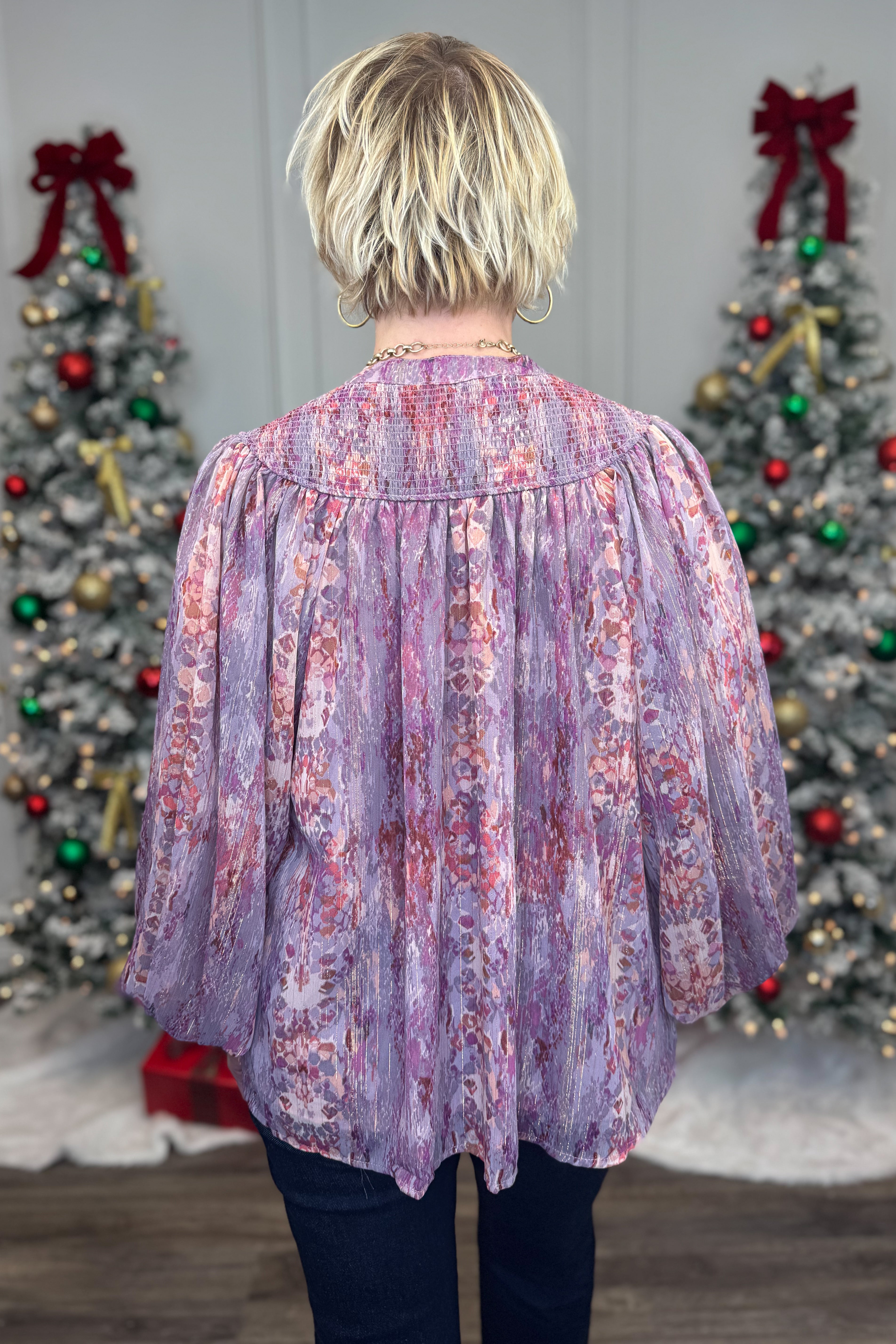 Person wearing a floral blouse with Christmas trees decorated with red bows in the background