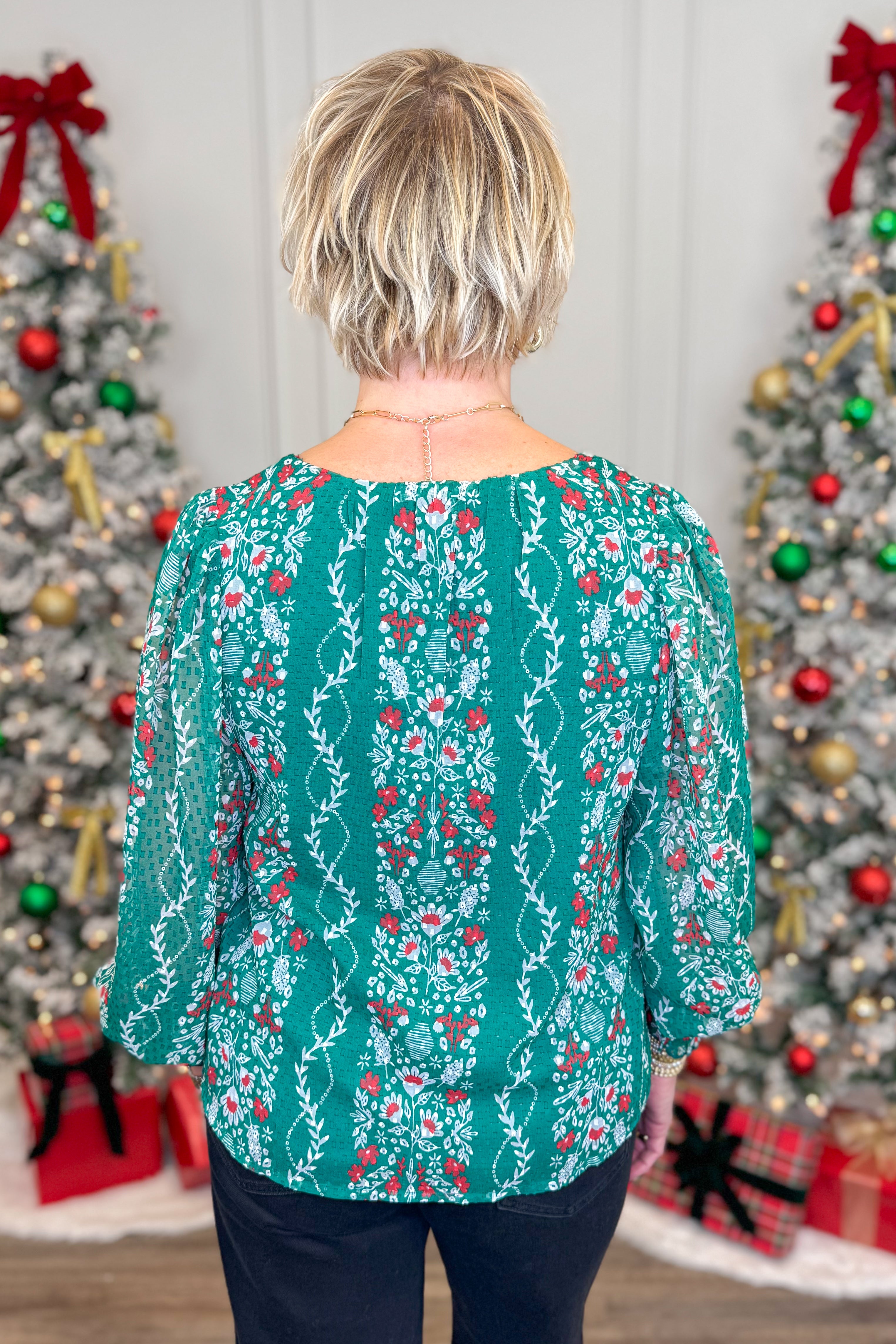 Person wearing a green patterned blouse with Christmas trees in the background