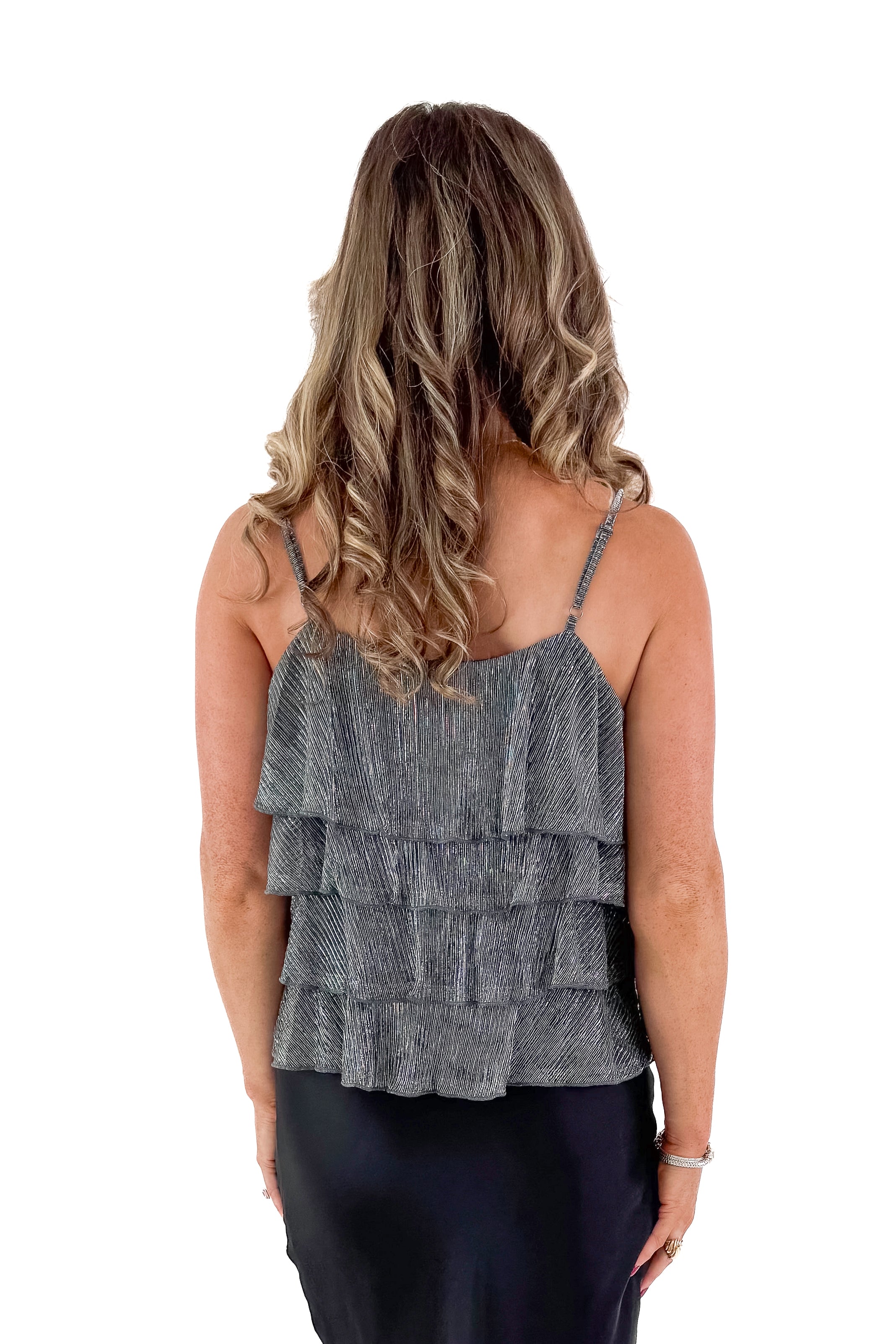 Back view of woman wearing Silver Metallic Ruffle Tank with black skirt against white studio background.