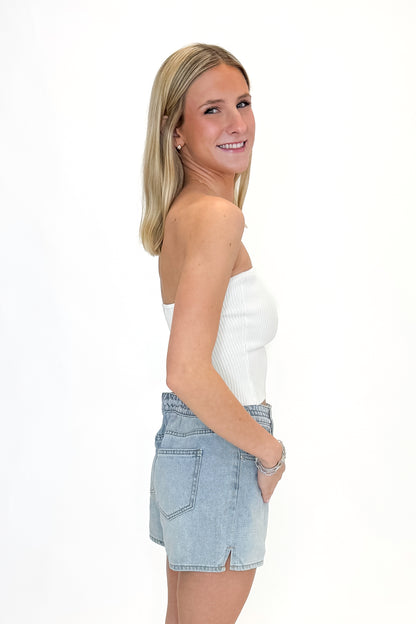 Side view of woman wearing Off White Ribbed Tube Top with jean shorts against white studio background.