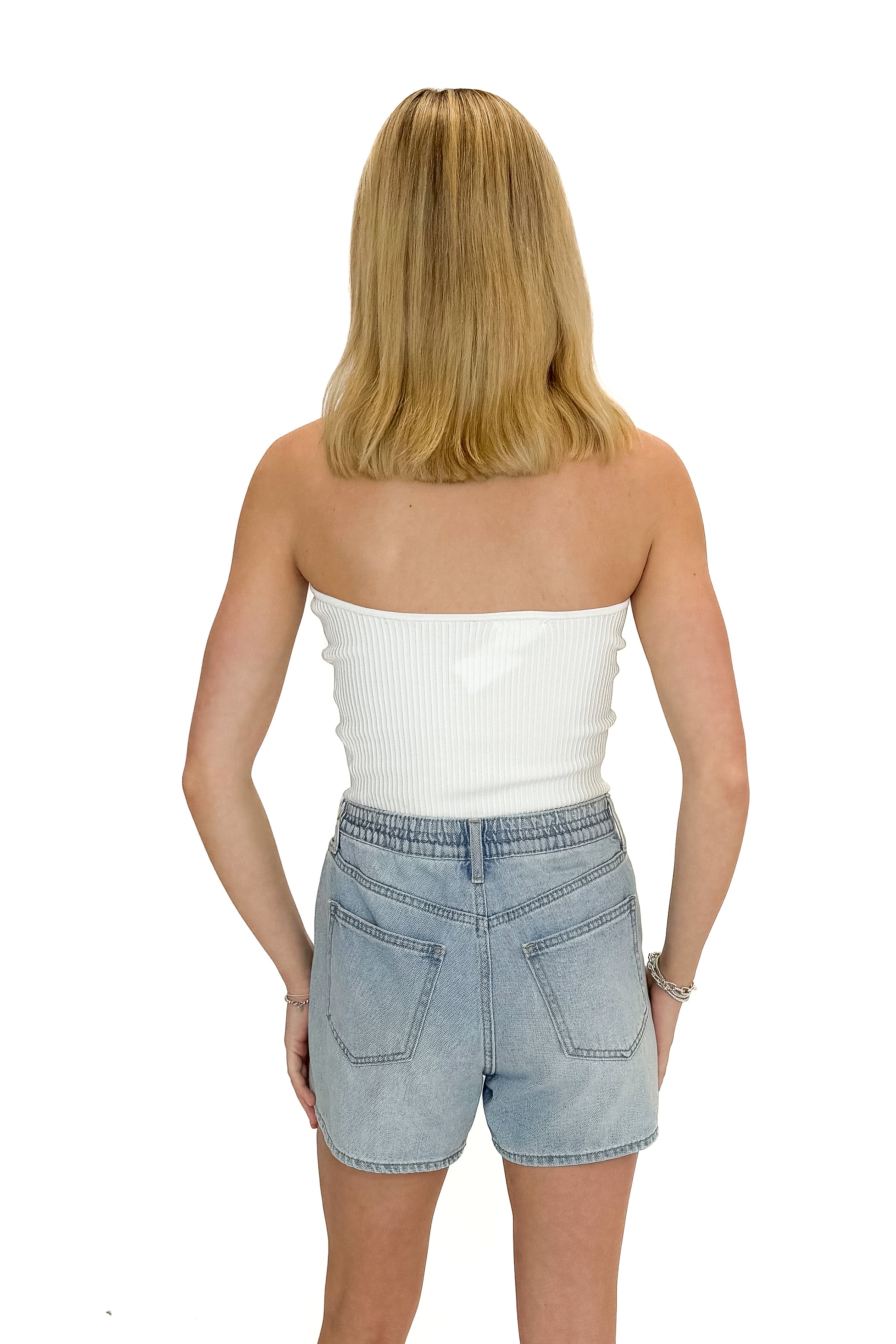 Back view of woman wearing Off White Ribbed Tube Top with jean shorts against white studio background.