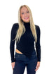 Front view of woman wearing Black Ribbed Asymmetrical Top with jeans against white studio background.