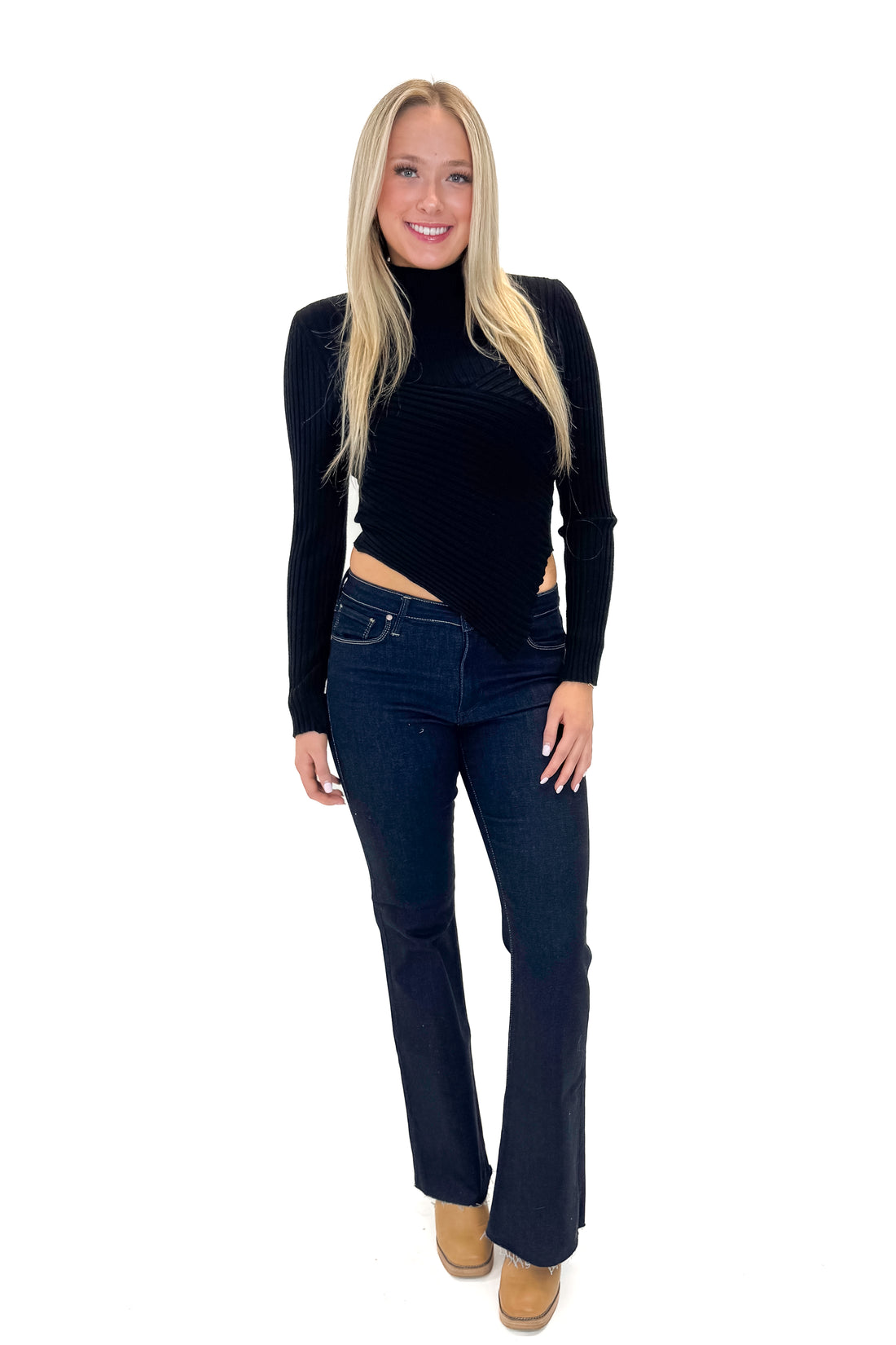 Front view of woman wearing Black Ribbed Asymmetrical Top with jeans against white studio background.